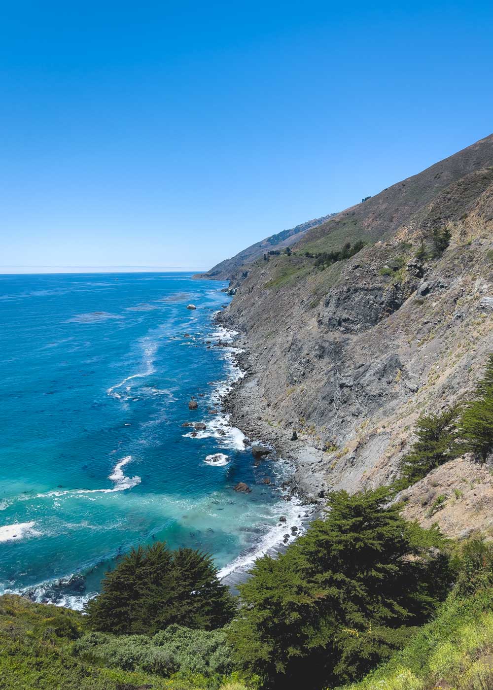 A view of cliffs and bright blue pacific ocean water from Ragged Point Trail on a clear clear.