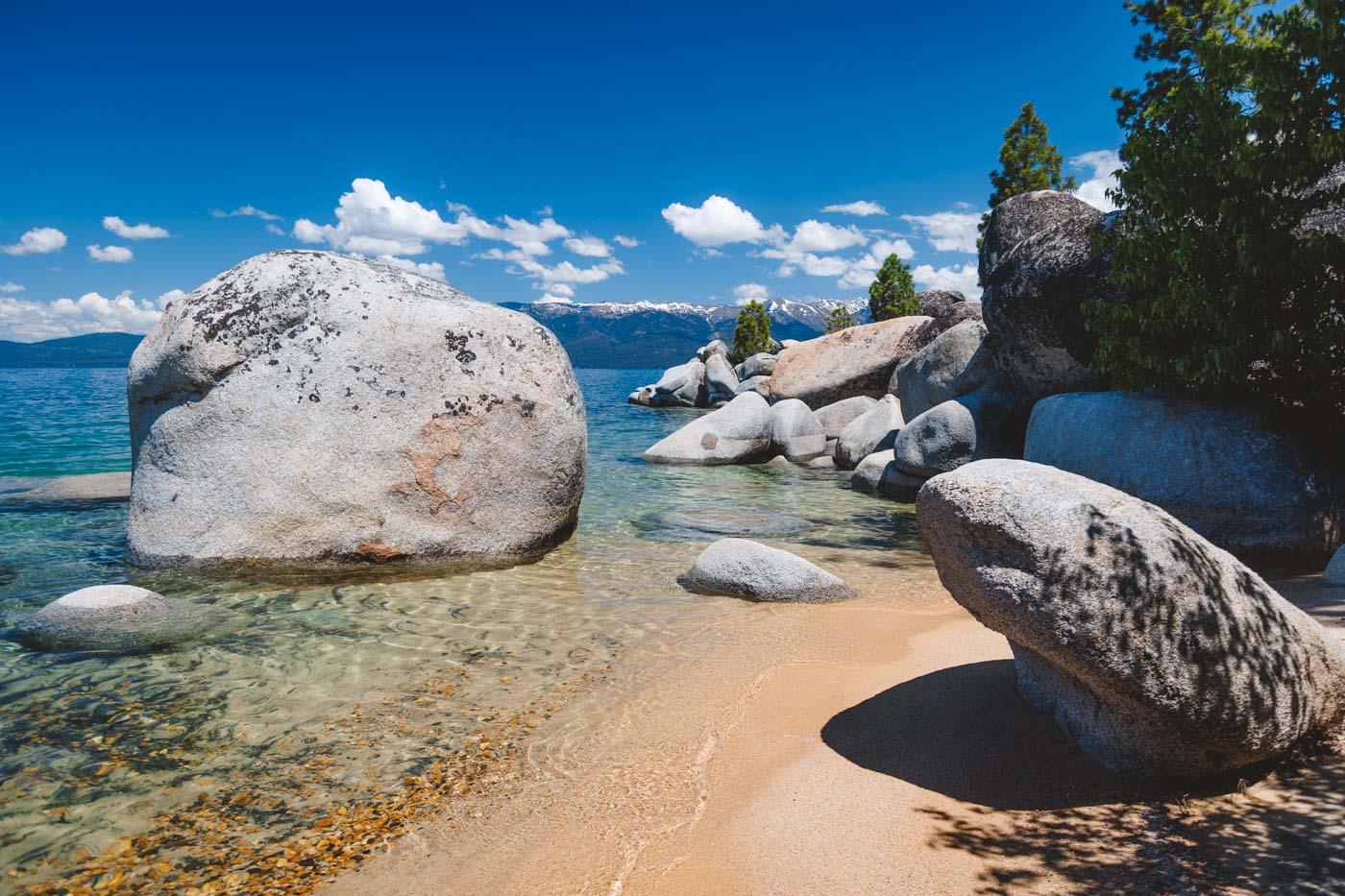 A view from standing on Whale Beach with smooth, round rocks on the beach and in Lake Tahoe on a sunny day.