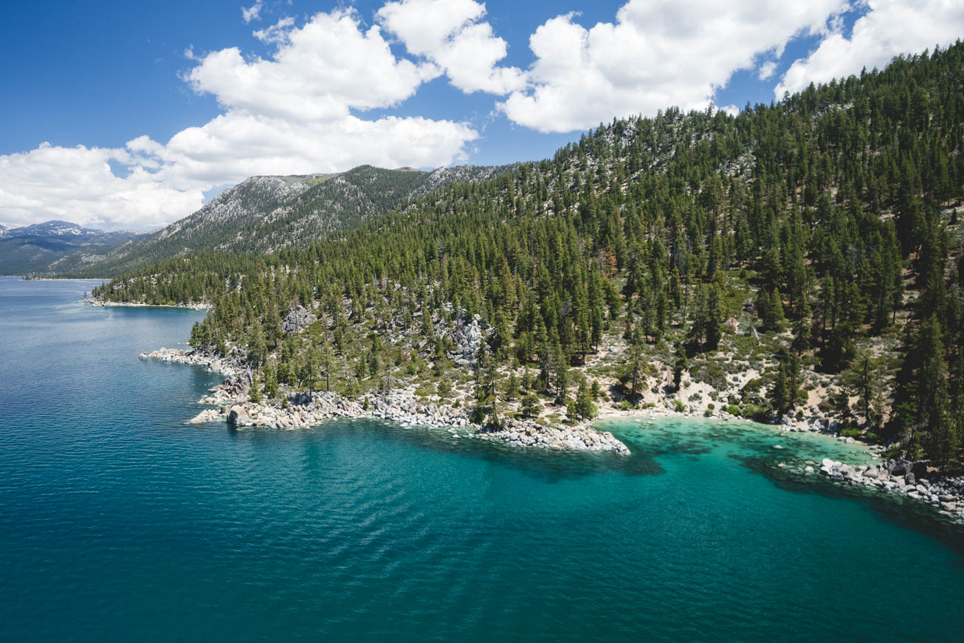 An aerial view of Secret Cove Beach along the shoreline of Lake Tahoe with trees lining the mountains around it.