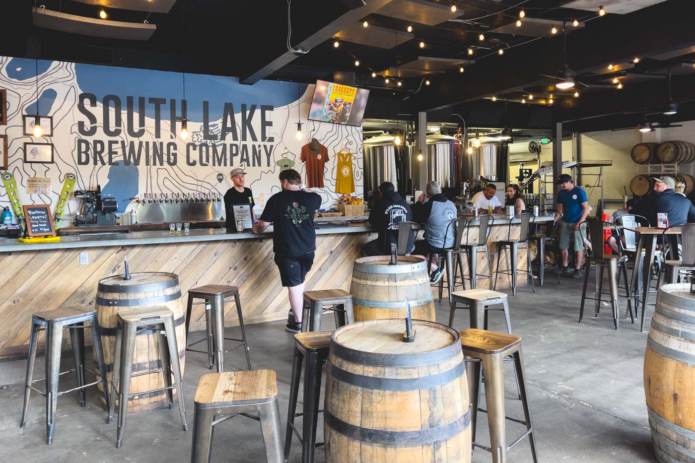 Customers inside South Lake Brewing Company sitting at the bar and on tables with decorative barrels around.