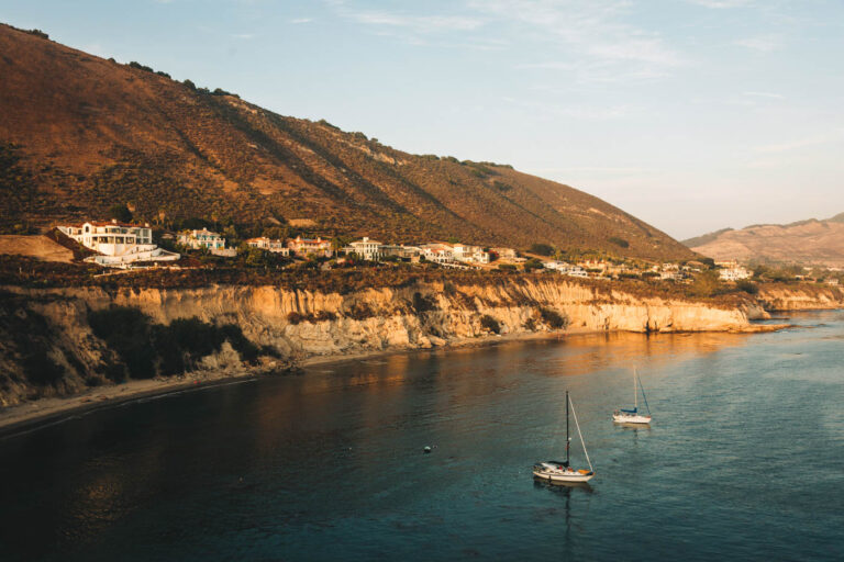 A beautiful golden sunset over Pirate Cove Beach with two sail boats anchored off the coast and villas along the coastline.