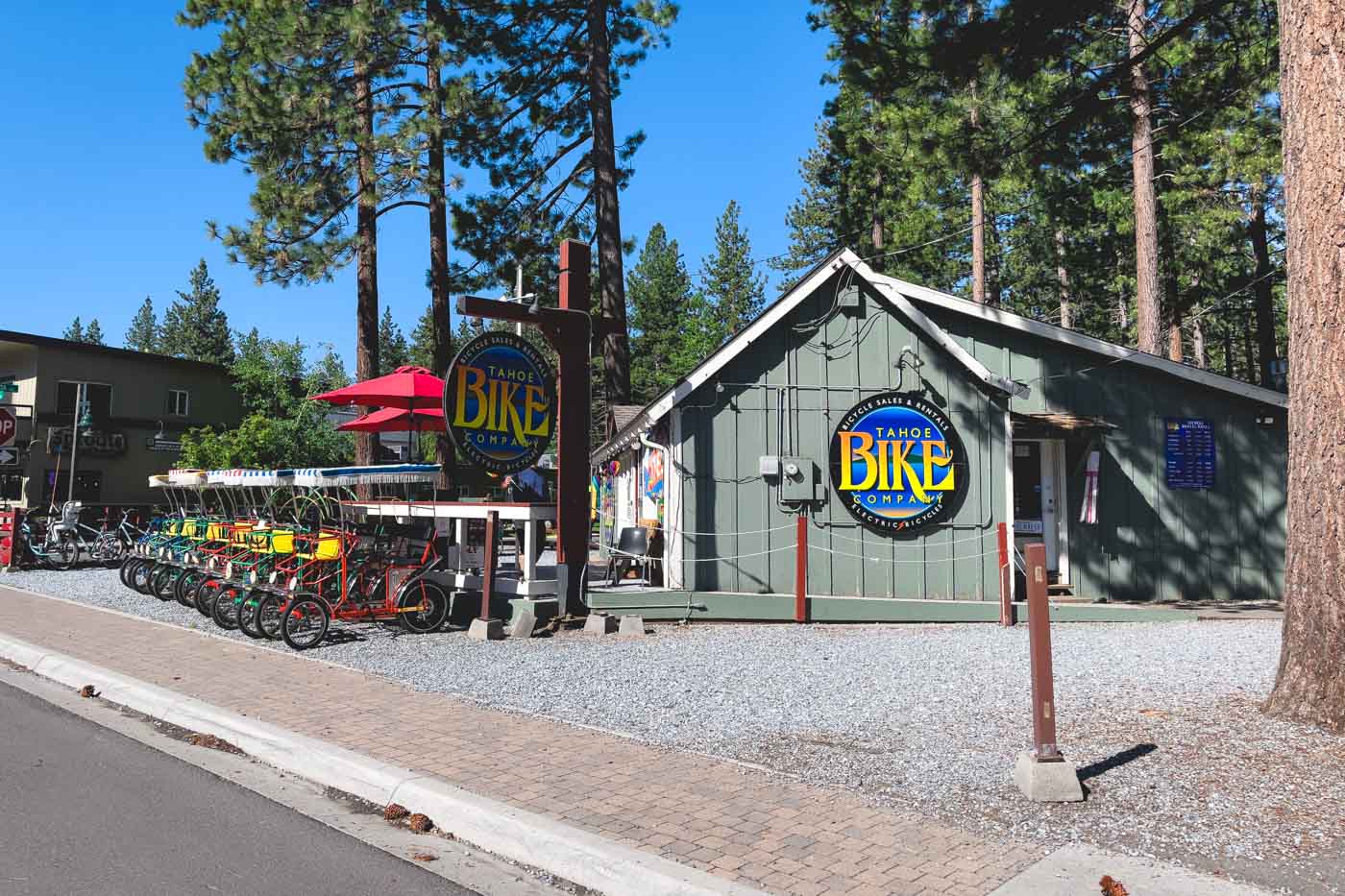 The exterior of Tahoe Bike company seen from the road with trees behind it on a sunny day in South Lake.