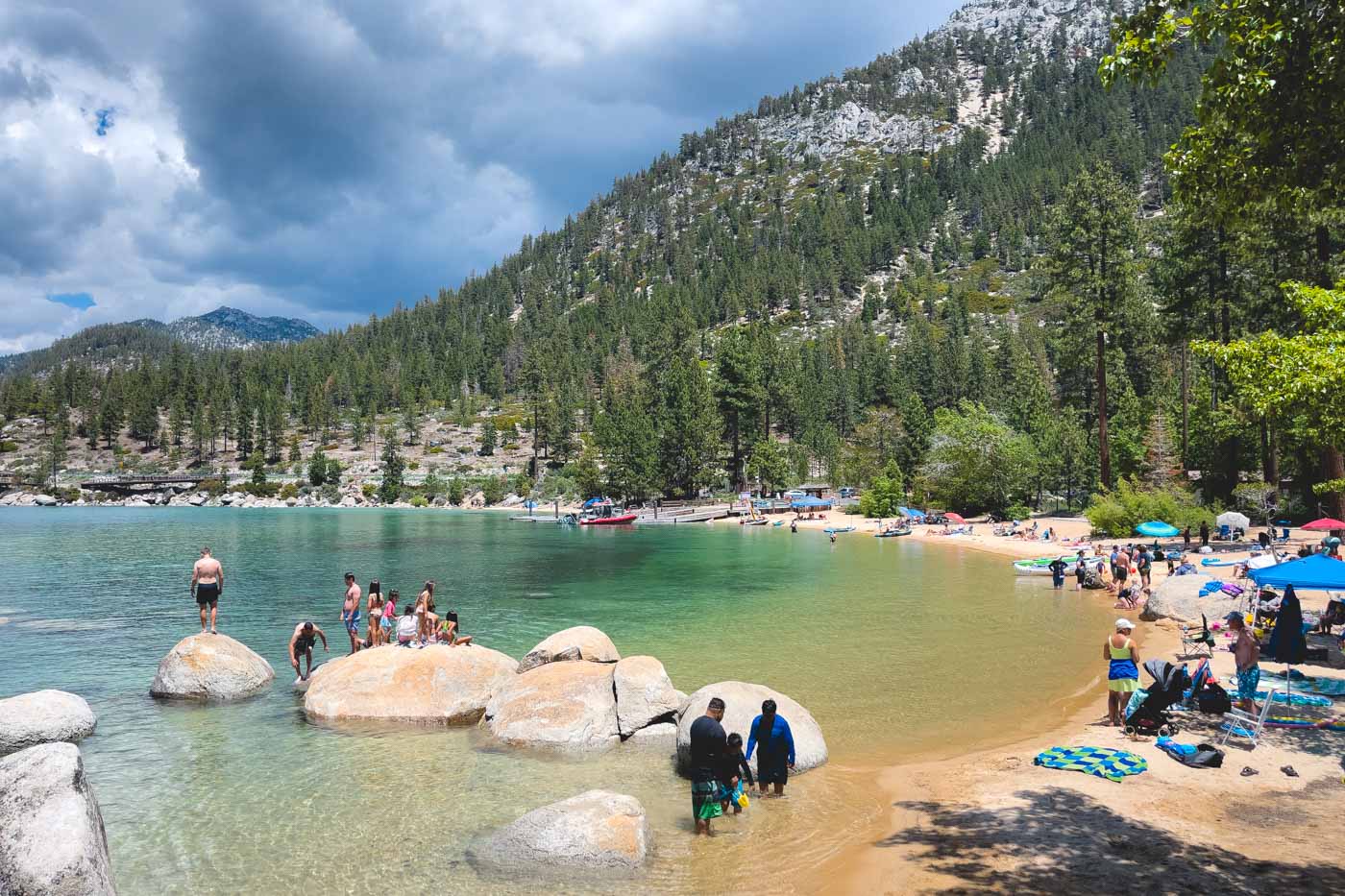 Tourists swimming in Lake Tahoe at Sand Harbor Beach with boats and kayak while standing on rocks in the water.