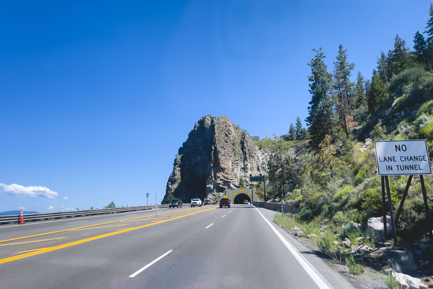 Driving down a highway beside Lake Tahoe and heading through a tunnel that leads through the giant Cave Rock on a sunny day.