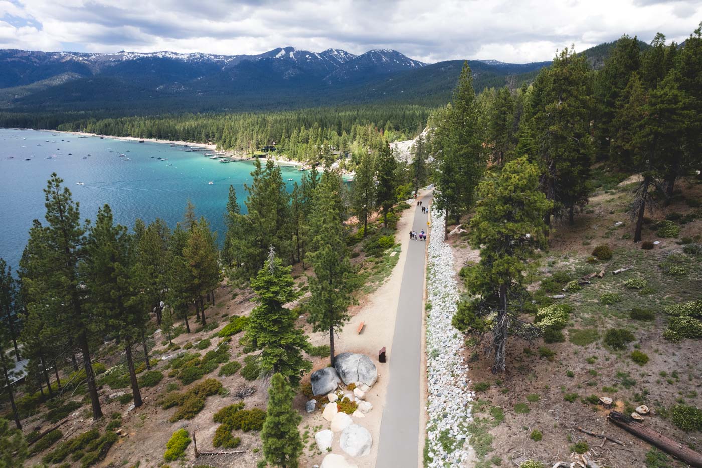 Aerial view overlooking the Tahoe East Shore Trail as people walk along the paved pathway between trees with a view of Lake Tahoe to the left.