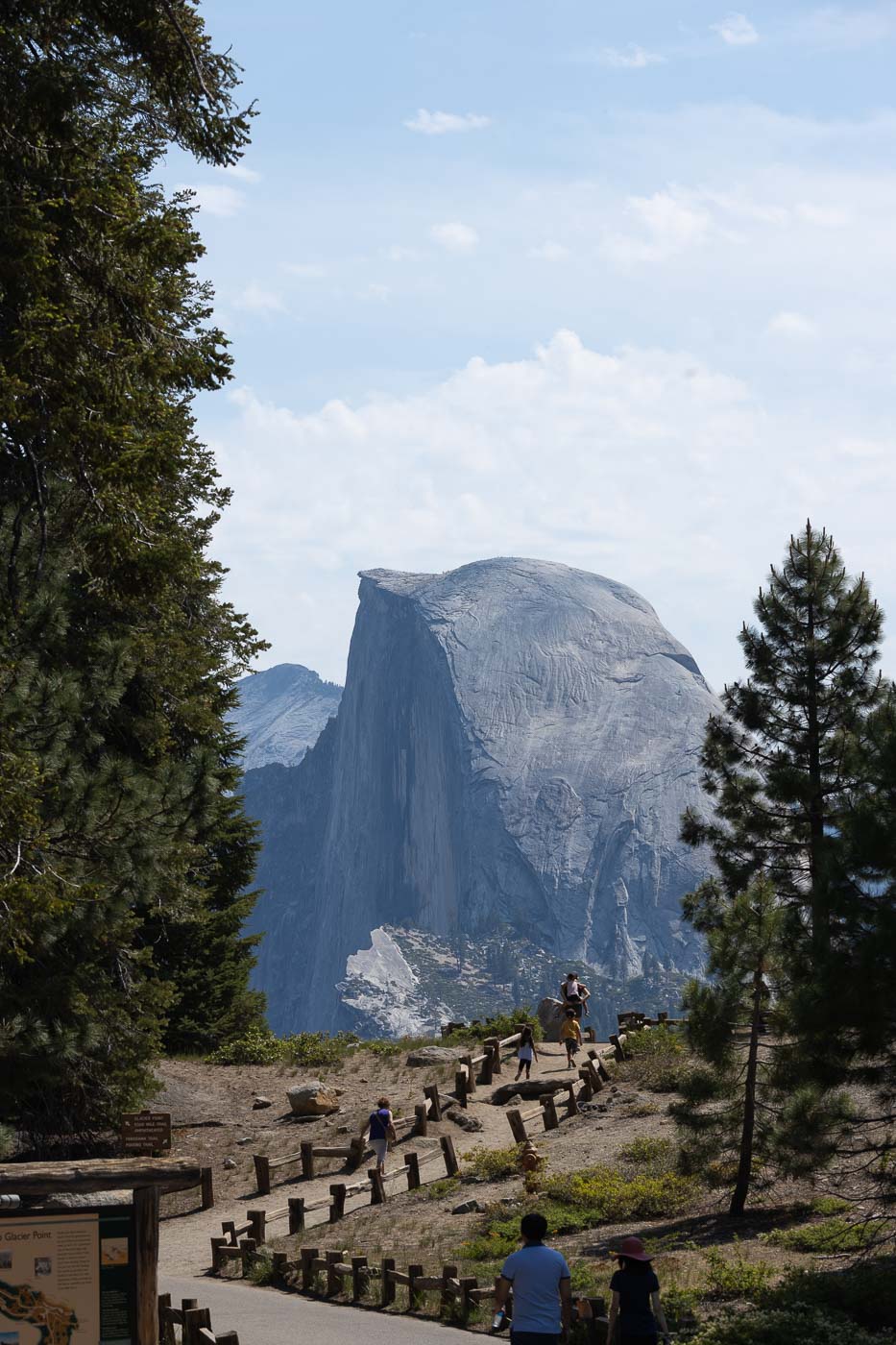 People strolling along a path at Glacier Point, Half Dome looms in the distance.