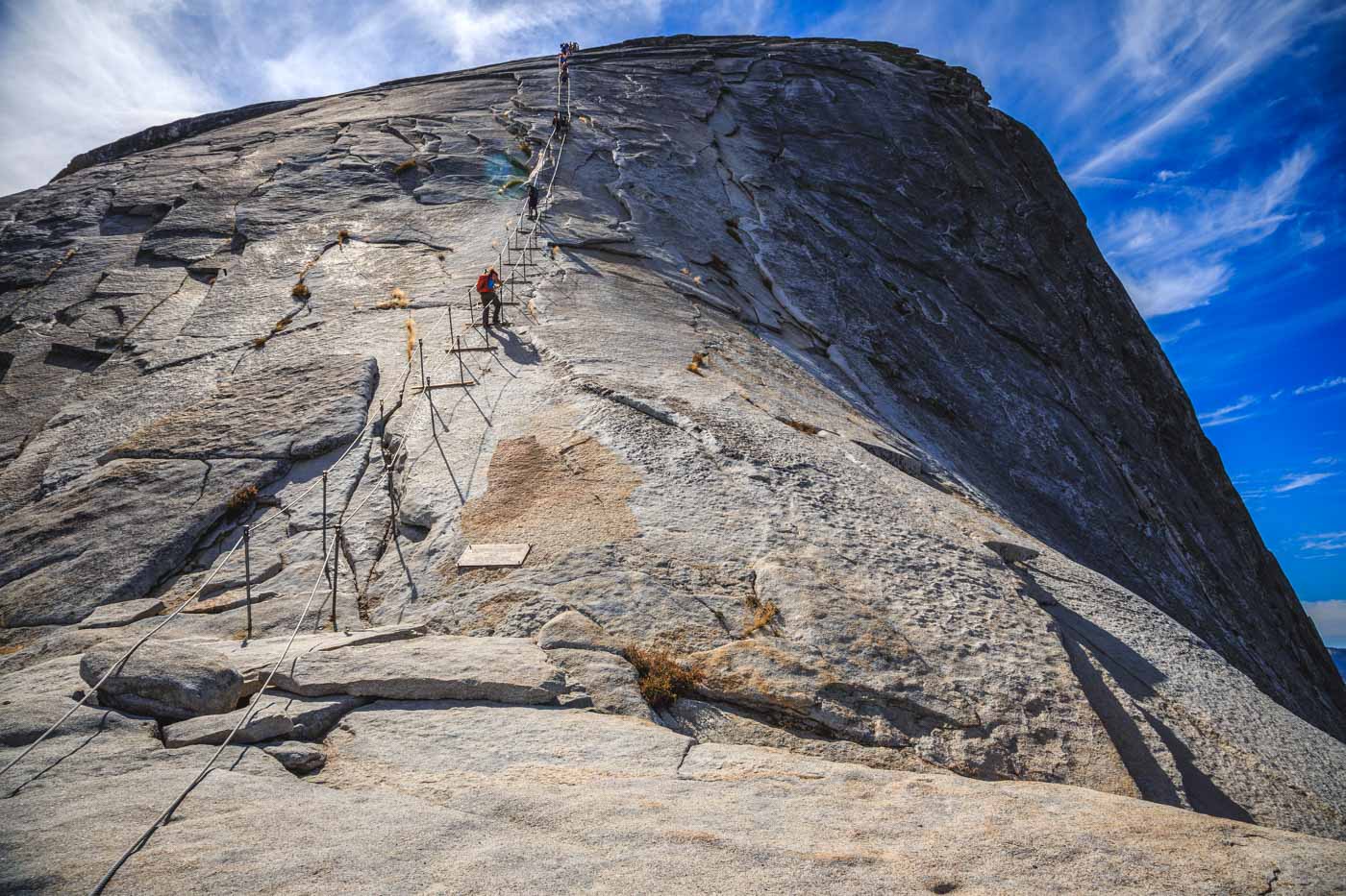 People scaling the side of Half Done using cables and wires in Yosemite.
