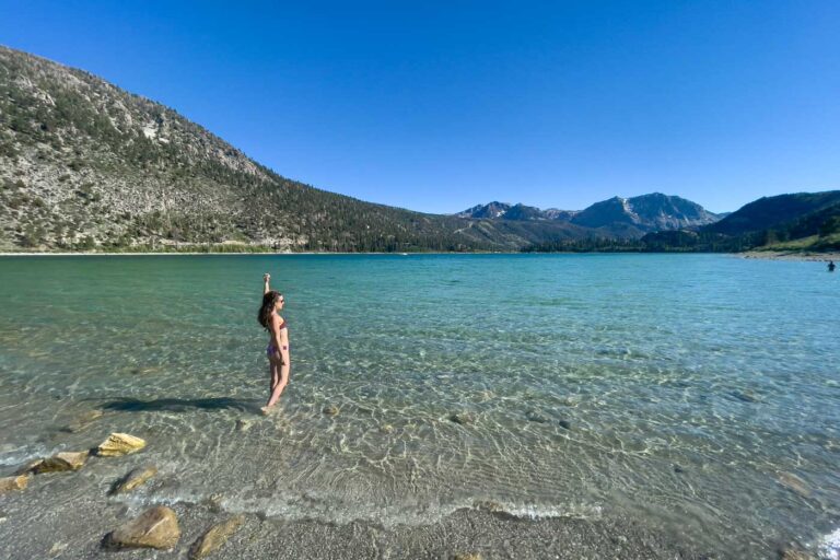 Nina in a swimsuit walking into June Lake on a sunny day with mountains the front.
